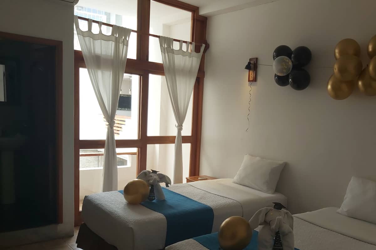 A hotel room with two beds, a large window with curtains, a wall clock, and balloons.