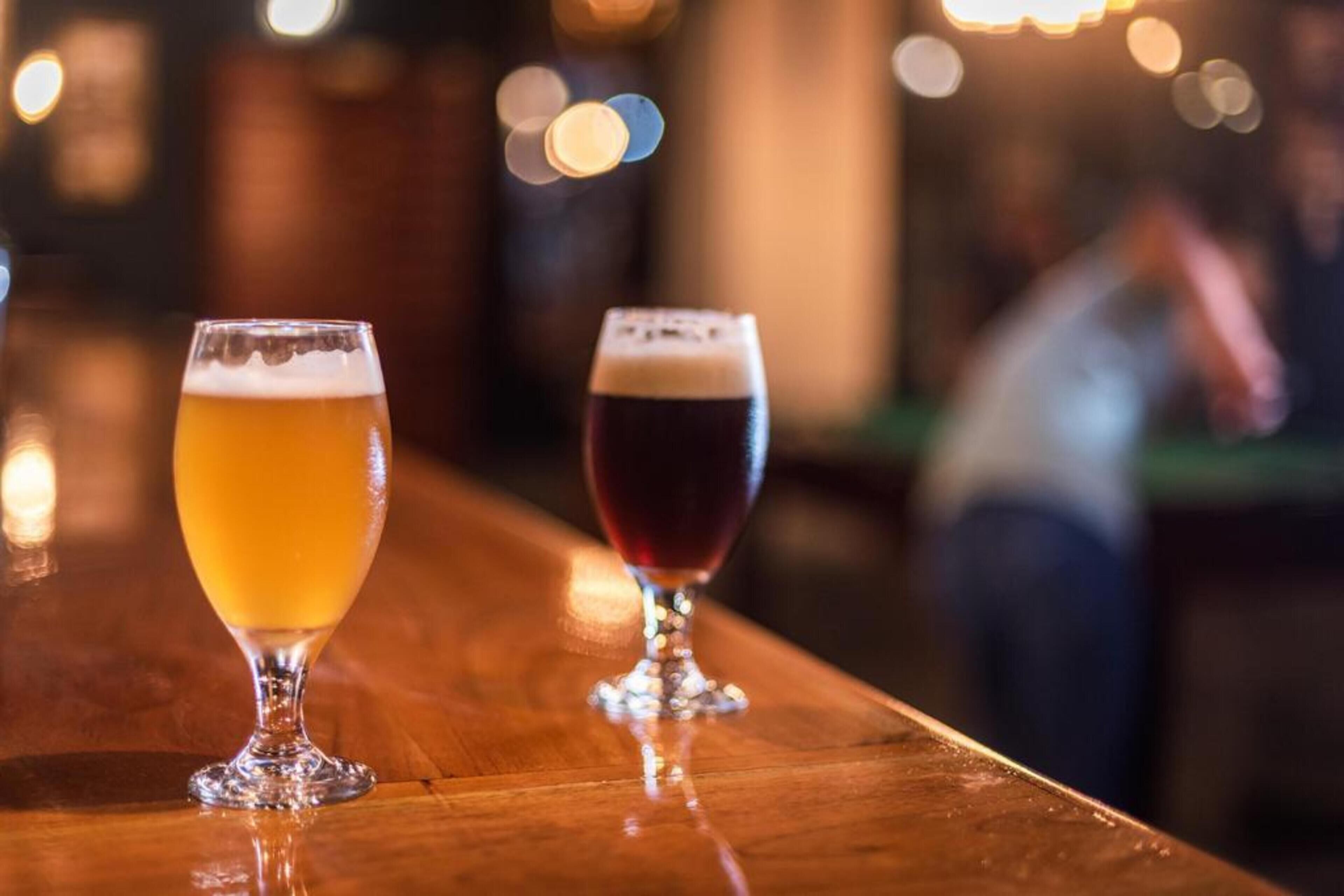 Two glasses of beer on a bar counter.