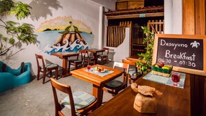 A restaurant with wooden tables and chairs, a mural of a turtle on a rock, and a chalkboard sign indicating breakfast hours. - Galapagos Native (Puerto Ayora)