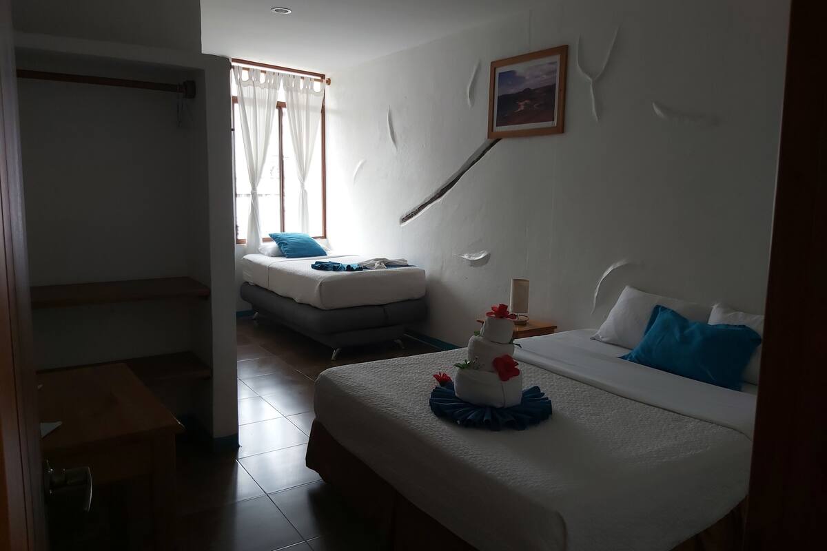 A hotel room with a bed, a nightstand, a window with curtains, and a painting on the wall.