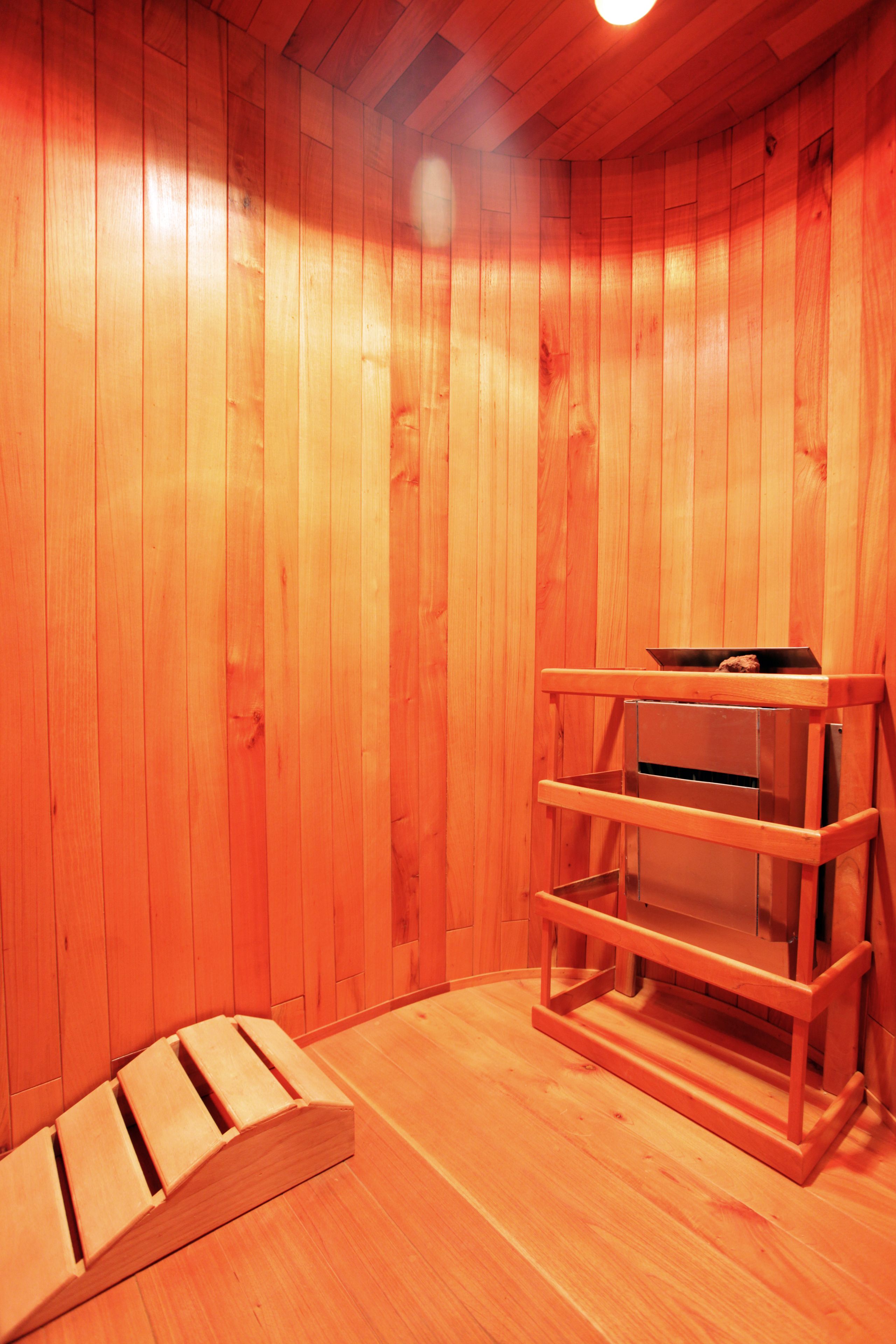 A wooden sauna room with a bench, a shelf, and a small heater.