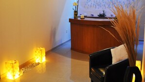 A reception area with a wooden reception desk, a black leather chair with a pillow, a television mounted on the wall, and a decorative wall with hanging elements. - Gran Casa Sayula Hotel & Spa (Sayula)