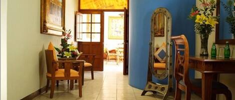 A room with a wooden dining table, chairs, a mirror, and a vase with flowers.