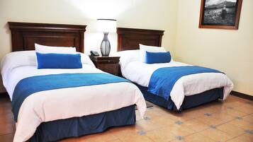 Dos camas dobles con ropa de cama azul y blanca, una mesita de noche con lámpara y un cuadro en la pared.