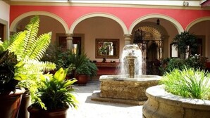 A courtyard with a fountain, potted plants, and a red building with arches. - Gran Casa Sayula Hotel & Spa (Sayula)