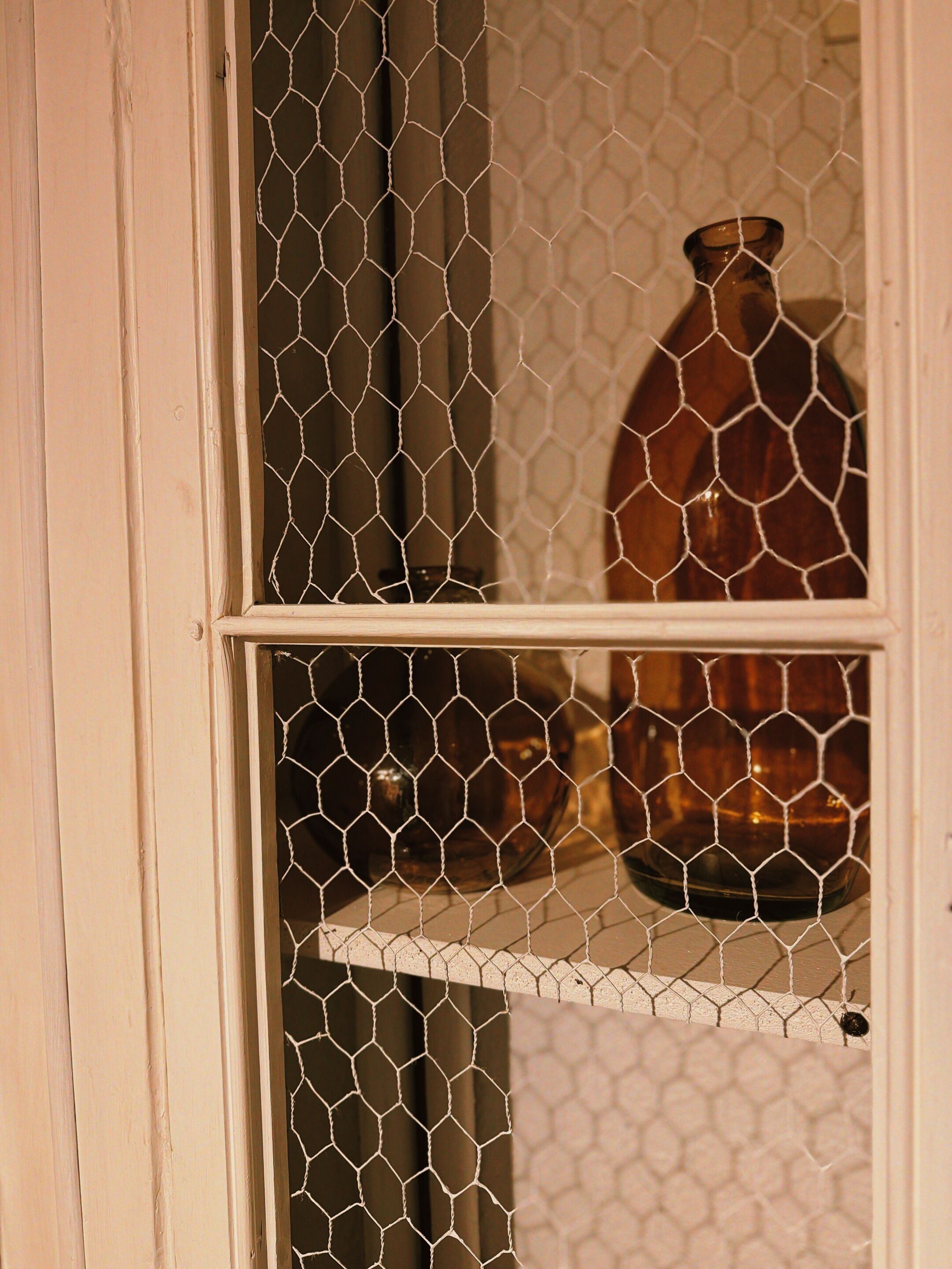 Una ventana con mosquitero, un estante con un recipiente de vidrio y un marco de puerta blanco.