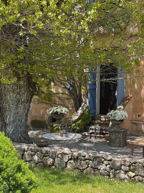 A stone wall, a tree, a metal table, and a building with a blue door. - La Bastide des Pins (La Bastide)