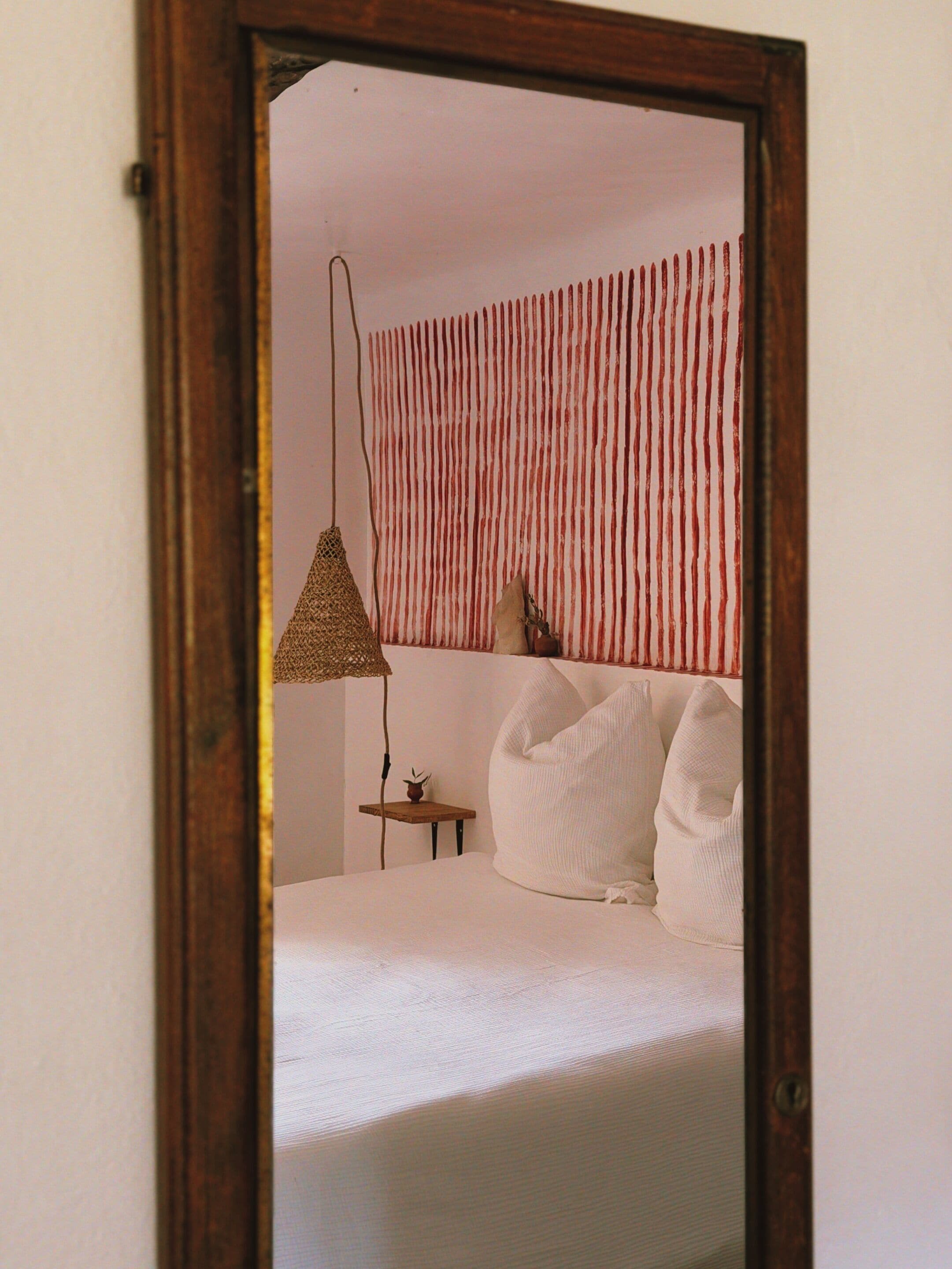 Une chambre à coucher avec un lit, des oreillers, une lampe suspendue et une petite table sur laquelle est posée une plante.