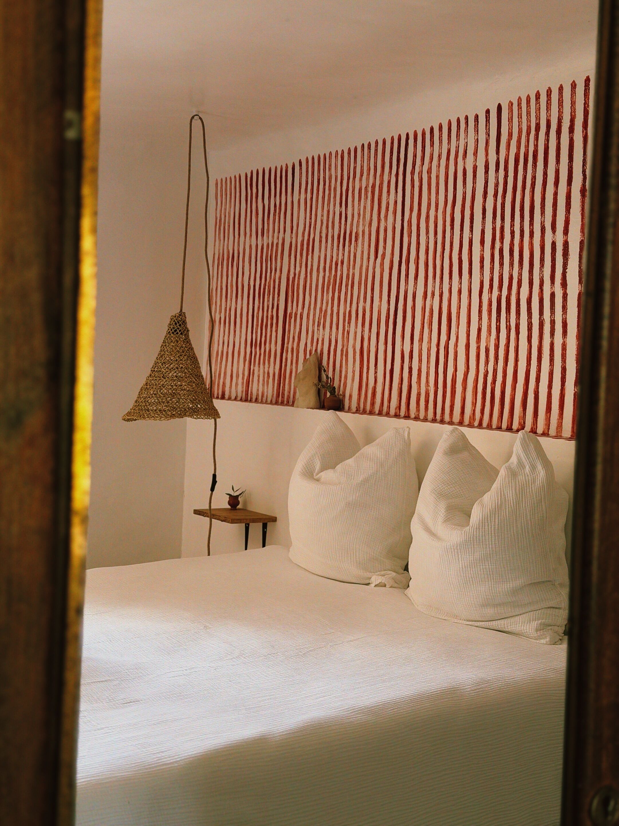 Une chambre à coucher avec un lit, des oreillers, une lampe suspendue, une petite table et un mur à rayures verticales.
