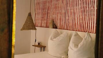 Une chambre à coucher avec un lit, des oreillers, une lampe suspendue, une petite table et un mur à rayures verticales.