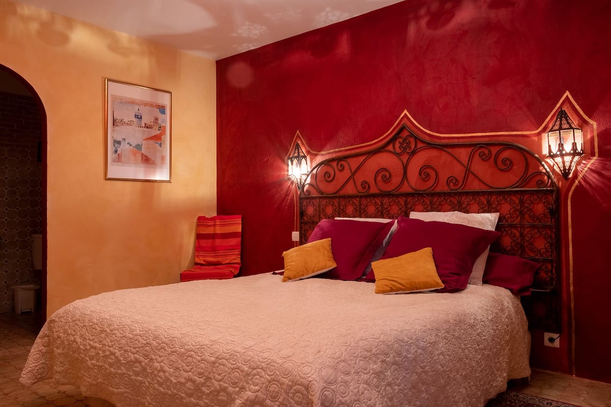 A bedroom with a red accent wall, a decorative headboard, and a framed picture on the wall.