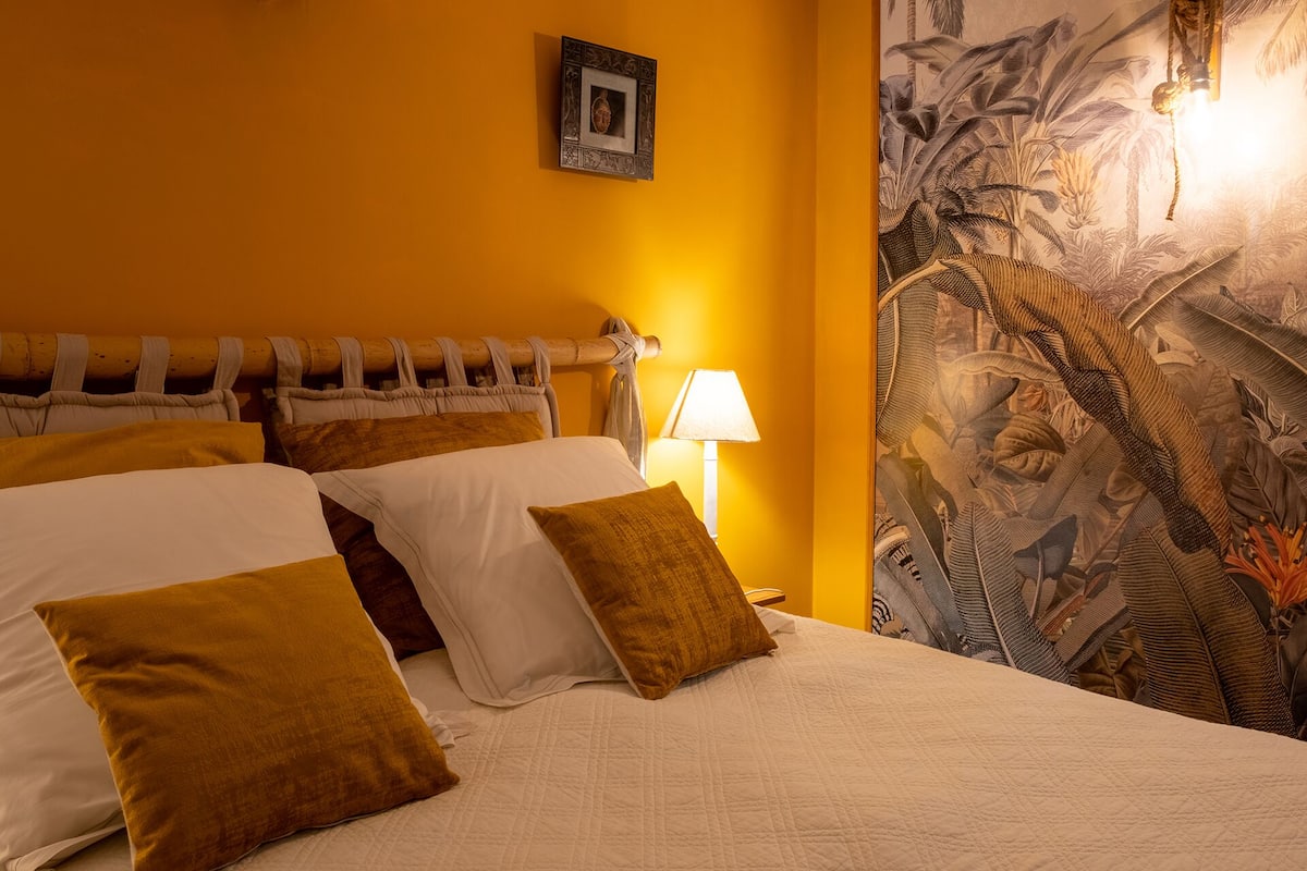 A hotel room with a large bed, a nightstand, a lamp, and a tropical mural on the wall.