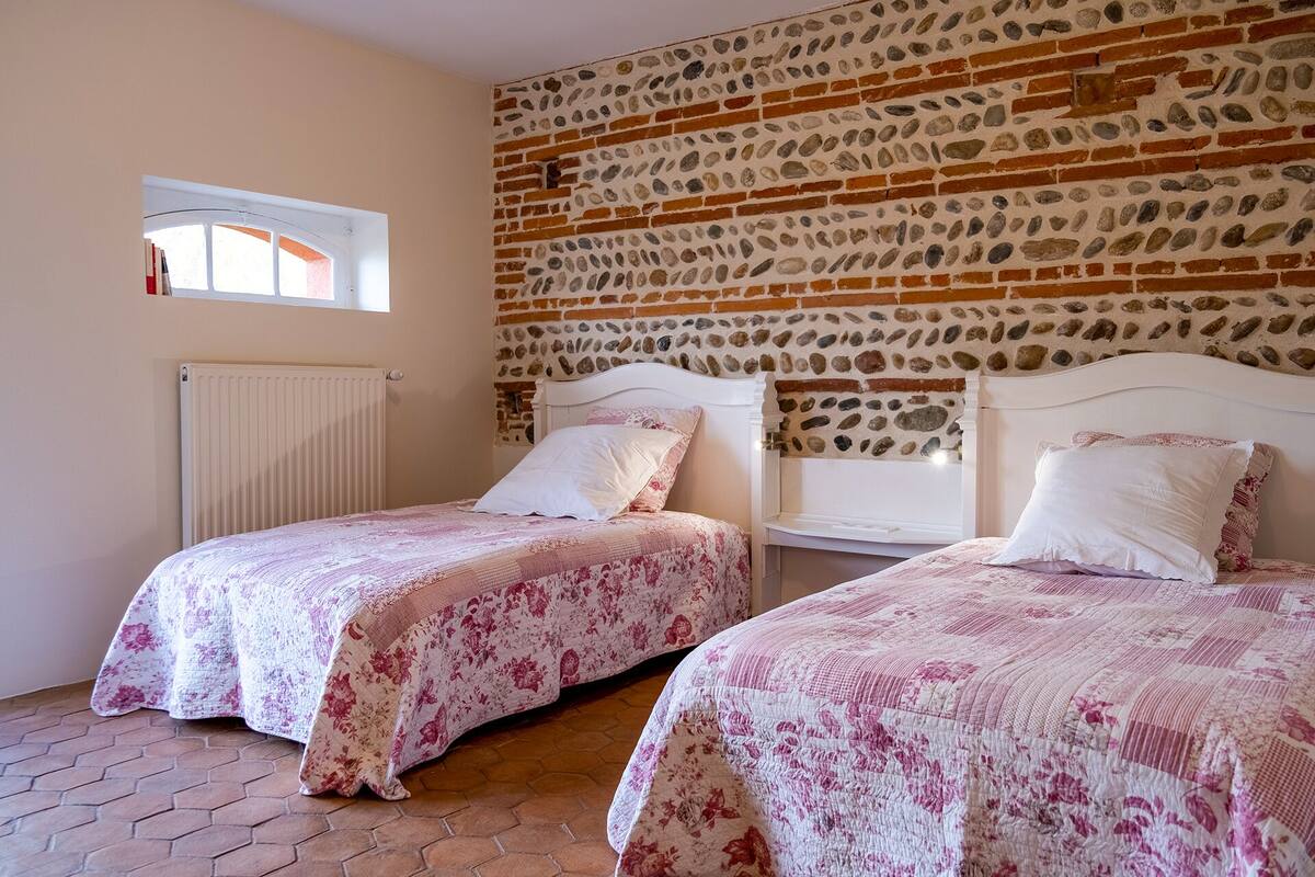 A bedroom with two beds, a stone wall, a window, and a radiator.
