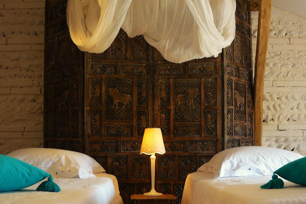 A room with two beds, a wooden floor, and a wall with carved panels.