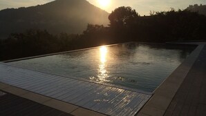 A swimming pool with a wooden deck and a view of the sun setting behind a hill.