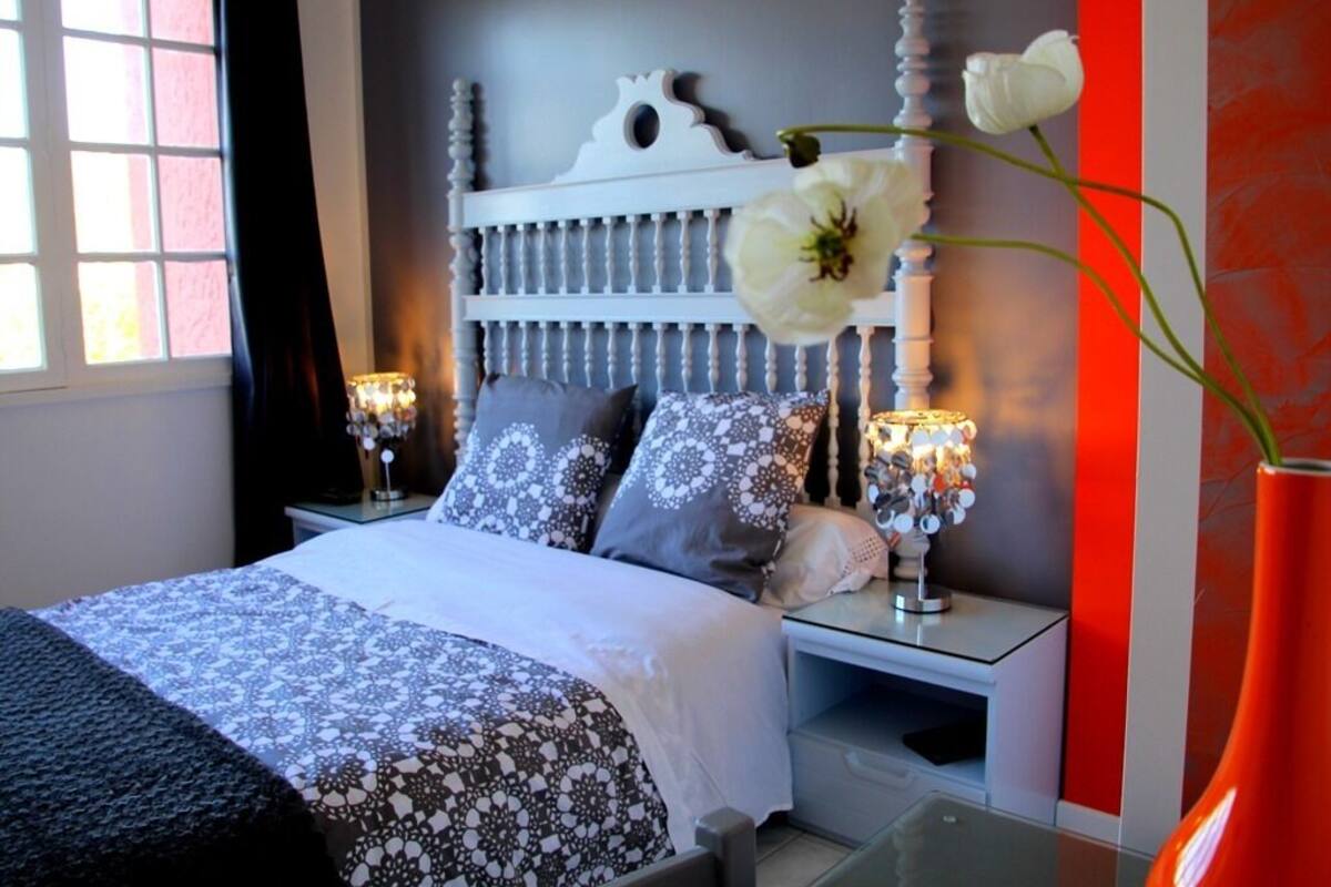 Ein Schlafzimmer mit einem Bett, Nachttischen, einer Lampe und einer Vase mit Blumen.
