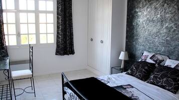 Een slaapkamer met een bed, een bureau, een stoel, een kledingkast en een raam met gordijnen.
