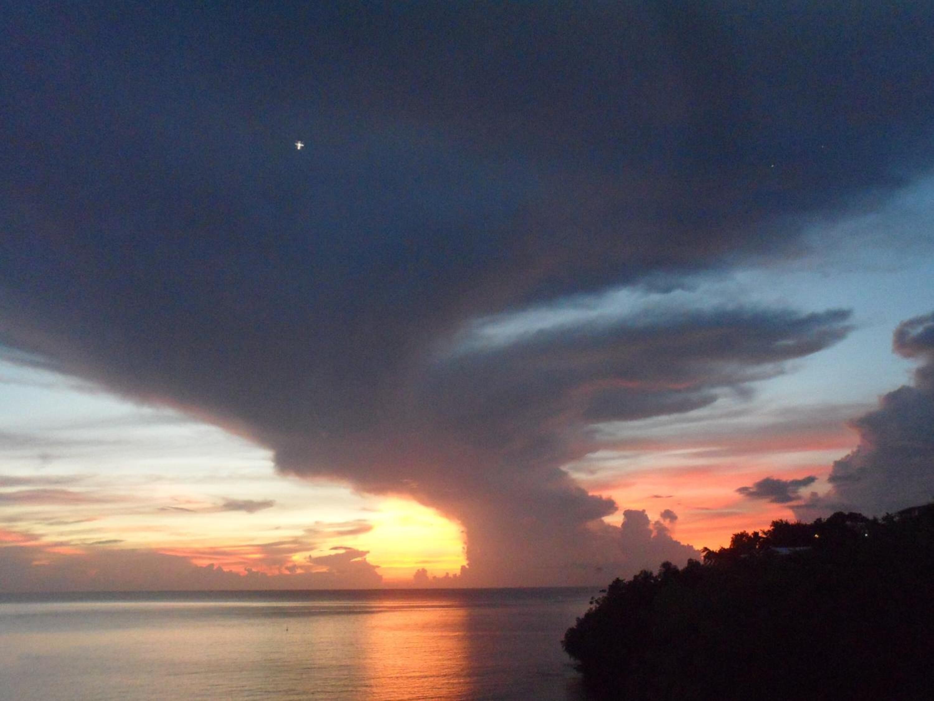 Un coucher de soleil sur une étendue d’eau, avec la silhouette d’une masse terrestre sur la droite.