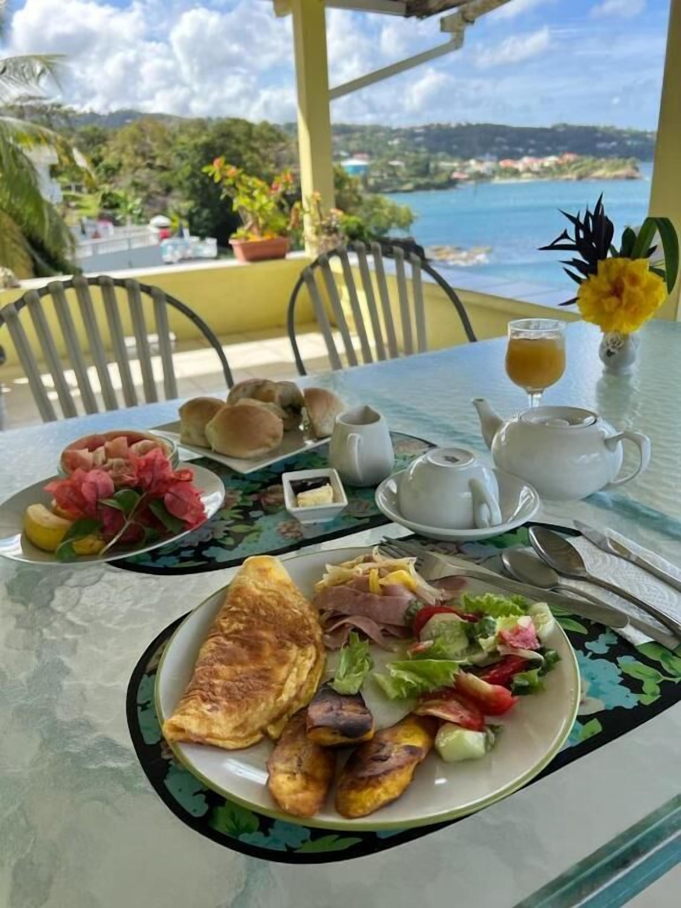 Mesa posta para o café da manhã, com torradas, ovos e frutas, e uma vista panorâmica ao fundo.