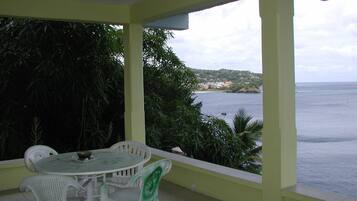 Un espace extérieur abrité, avec une table et des chaises, offrant une vue sur une étendue d’eau et une côte lointaine.