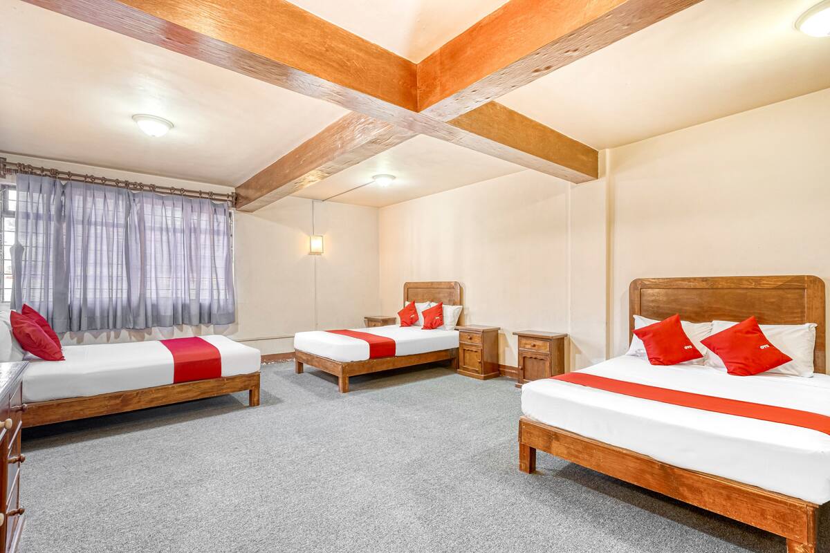 Une chambre d’hôtel avec trois lits en bois, chacun agrémenté de draps blancs et de touches de couleur rouge, un plafond en bois et un sol recouvert de moquette.