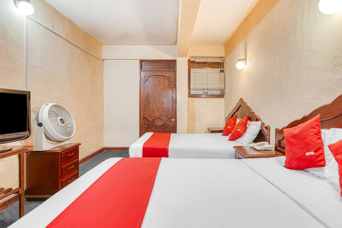 Une chambre d’hôtel avec deux lits, une télévision, un ventilateur et une armoire en bois.