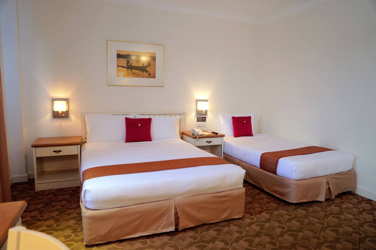 A hotel room with two beds, each with a red pillow, a nightstand with a lamp, and a framed picture on the wall.
