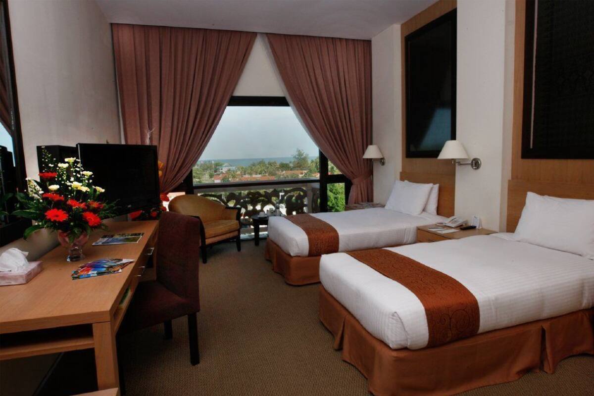 A hotel room with two beds, a desk, a chair, a TV, and a view of the outdoors.