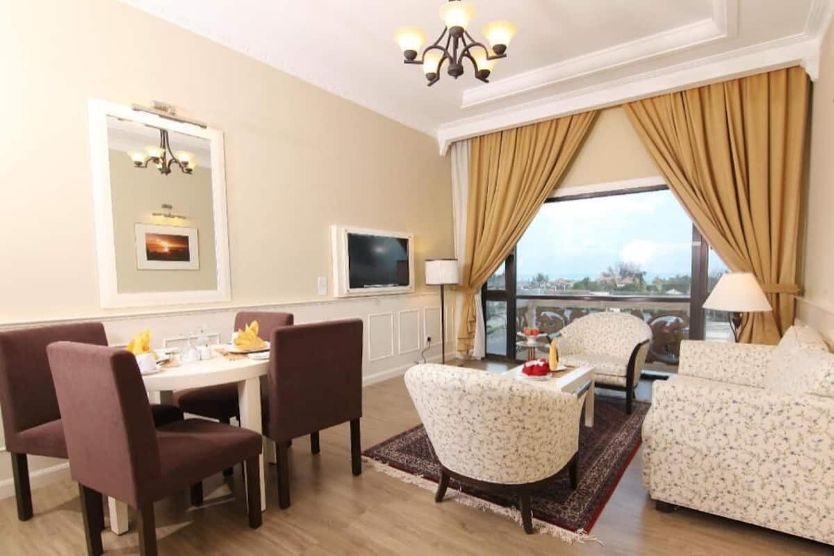 A hotel room with a dining area, a sofa, a TV, and a large window with curtains.