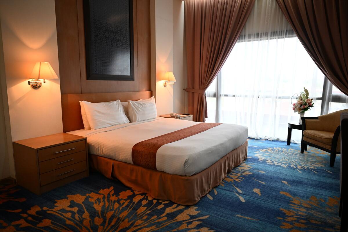 A hotel room with a large bed, two bedside tables, a nightstand, a chair, and a window with curtains.