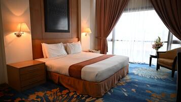 A hotel room with a large bed, two bedside tables, a nightstand, a chair, and a window with curtains.