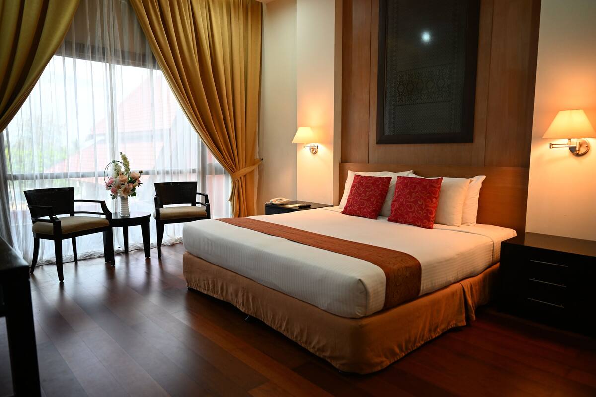 A hotel room with a large bed, two bedside tables, a desk with chairs, and a window with curtains.