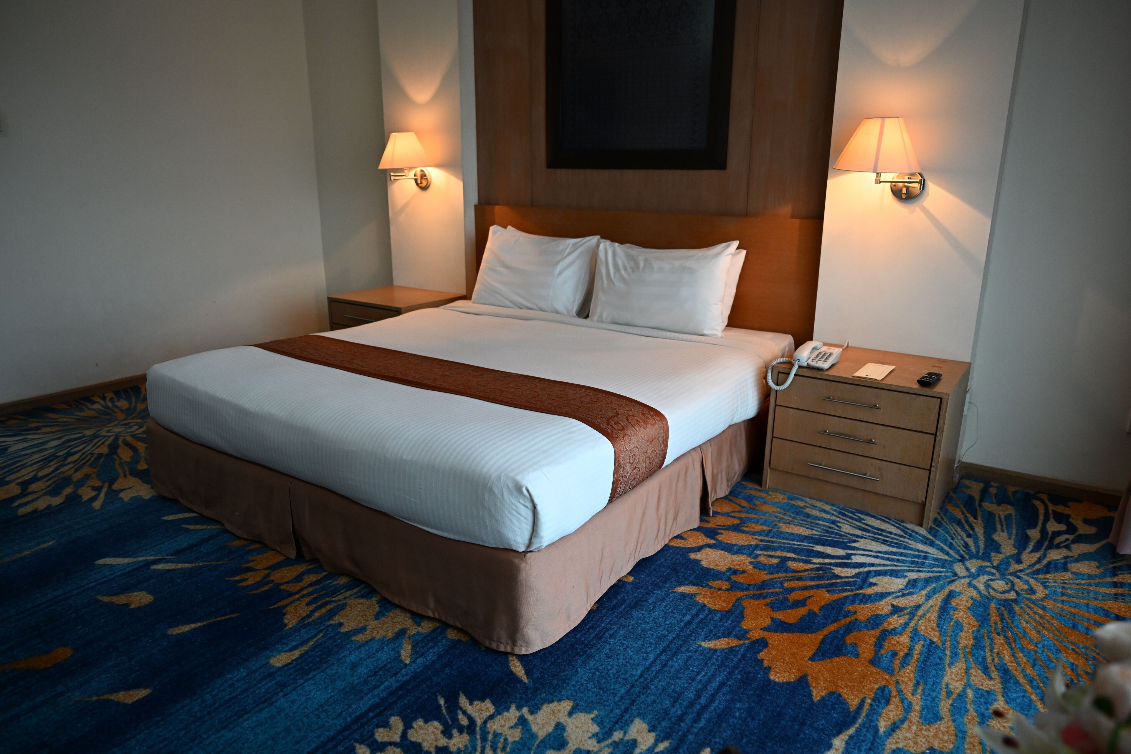 A hotel room with a large bed, two bedside tables, a nightstand, and a patterned carpet.