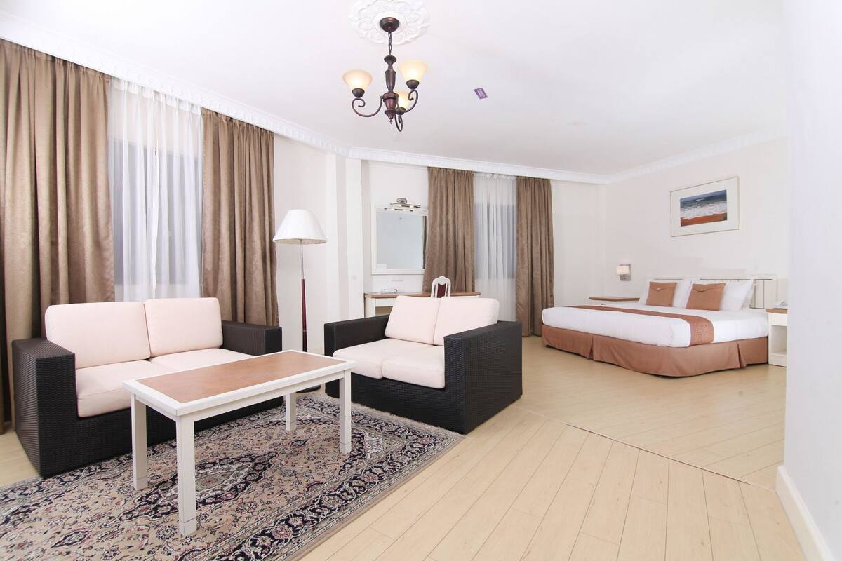 A hotel room with a sofa, a bed, a small table, a lamp, and a rug.