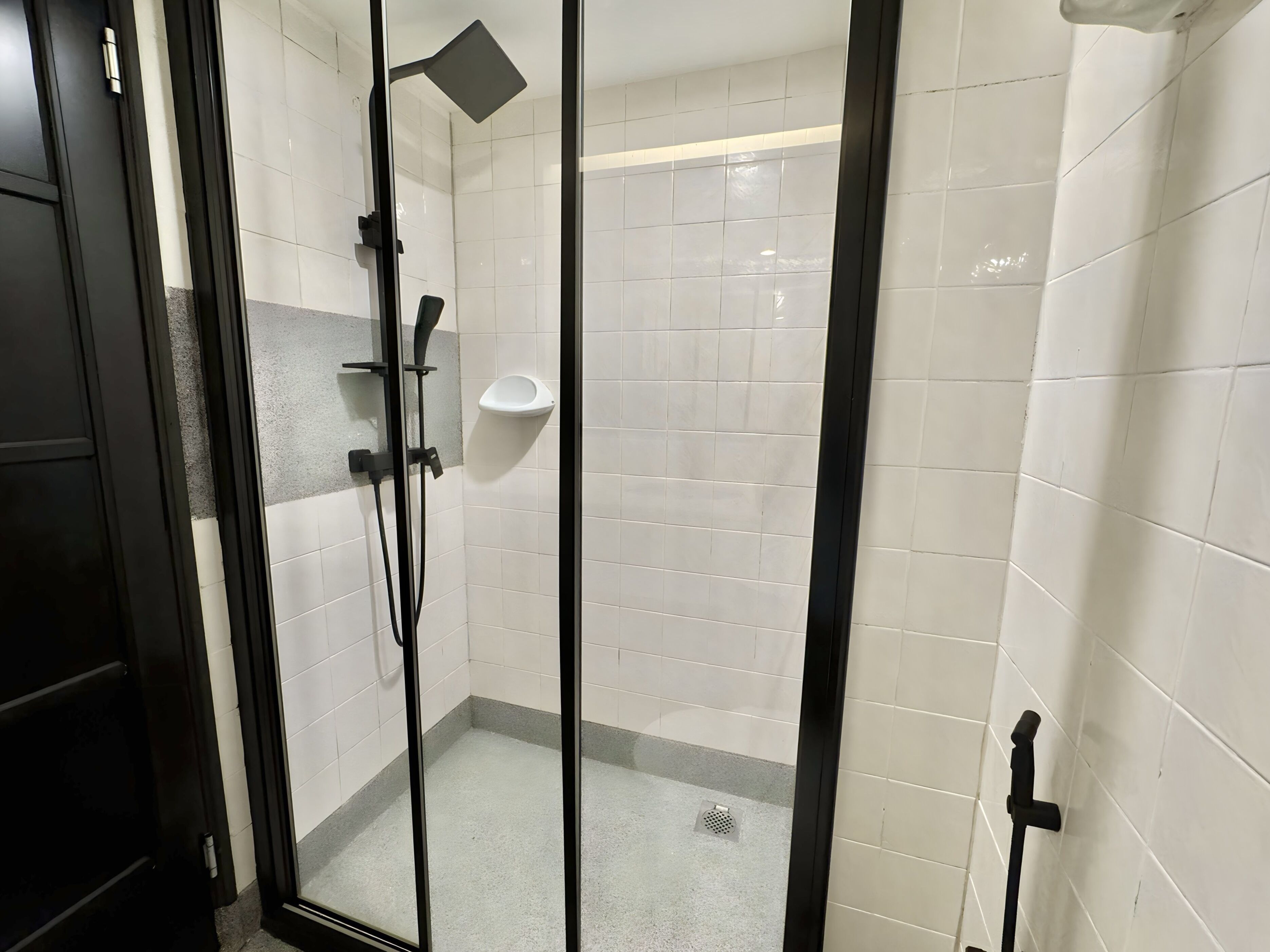 A glass-enclosed shower with white tiled walls, a handheld showerhead, and a handheld shower attachment.