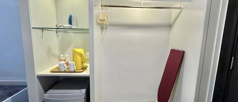 A compact hotel room with a built-in ironing station, a small shelf with toiletries, and a red folding chair.