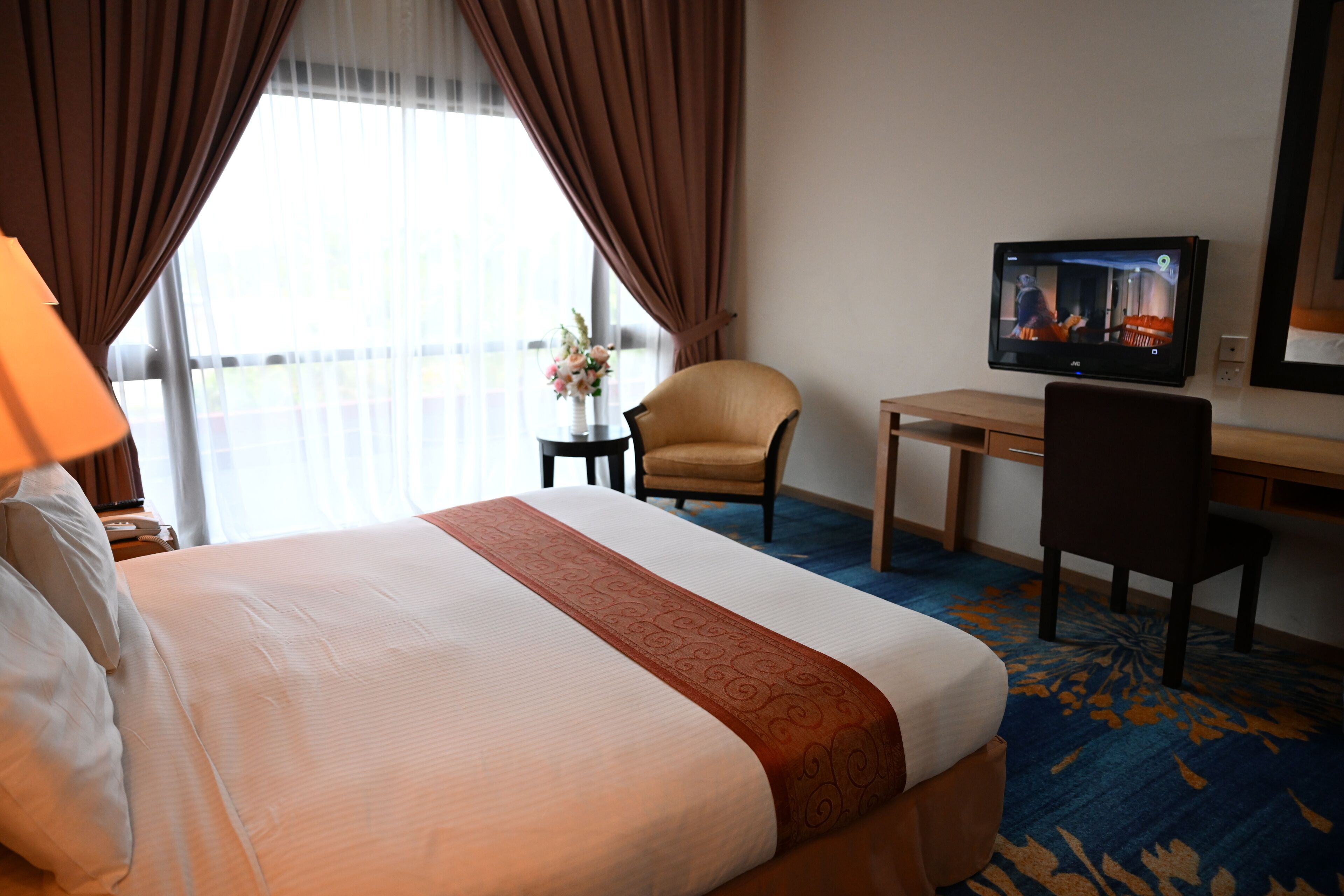 A hotel room with a large bed, a desk, a chair, a television, and a window with curtains.