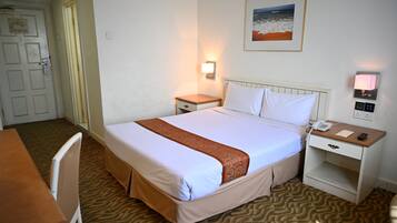 Ett hotellrum med en säng, ett sängbord, en nattdukslampa och ett skrivbord med en stol.