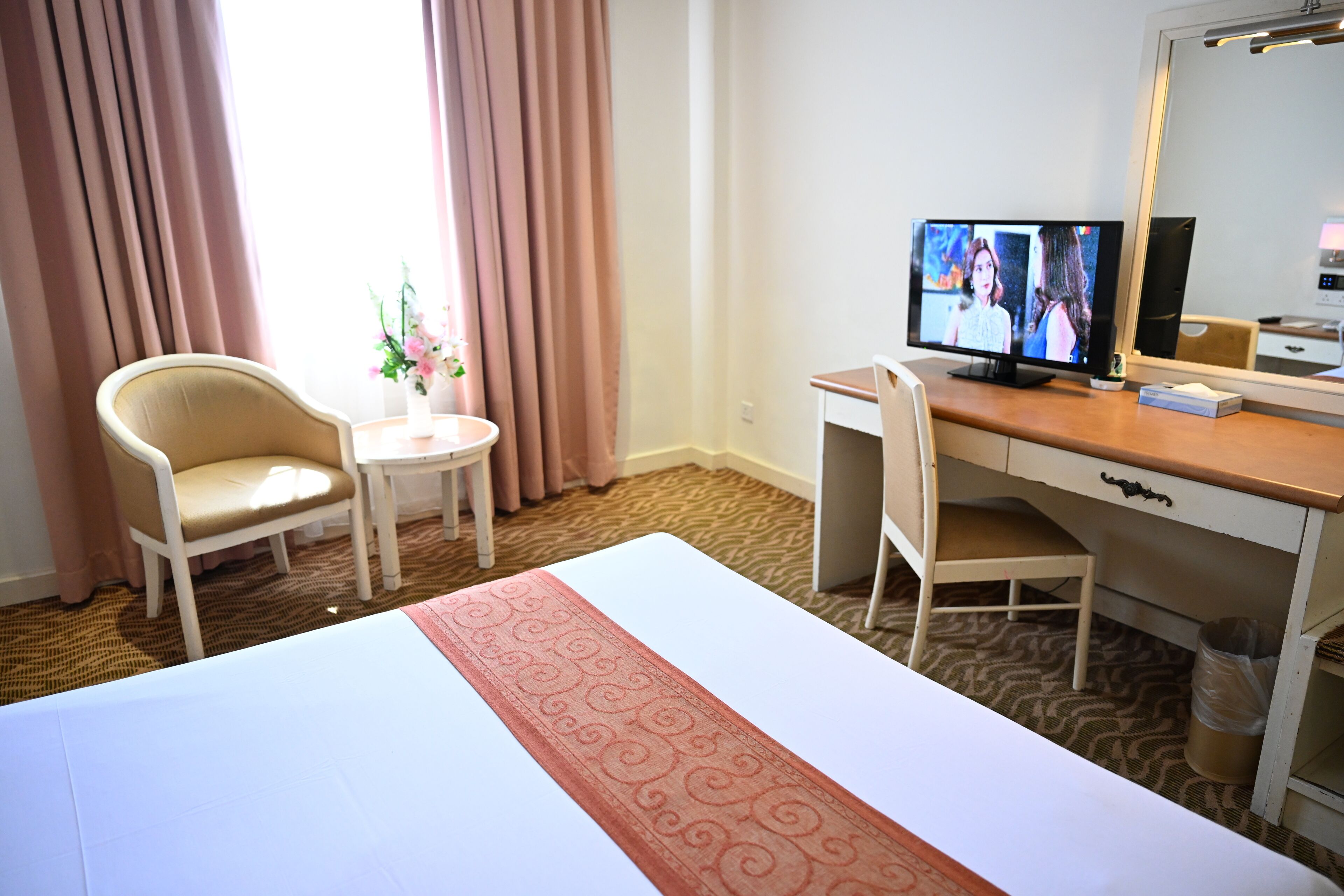A hotel room with a bed, a desk, a chair, a television, and a mirror.
