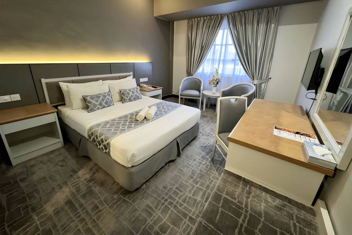A hotel room with a large bed, bedside tables, a desk with a chair, a small table with a vase of flowers, and a TV.