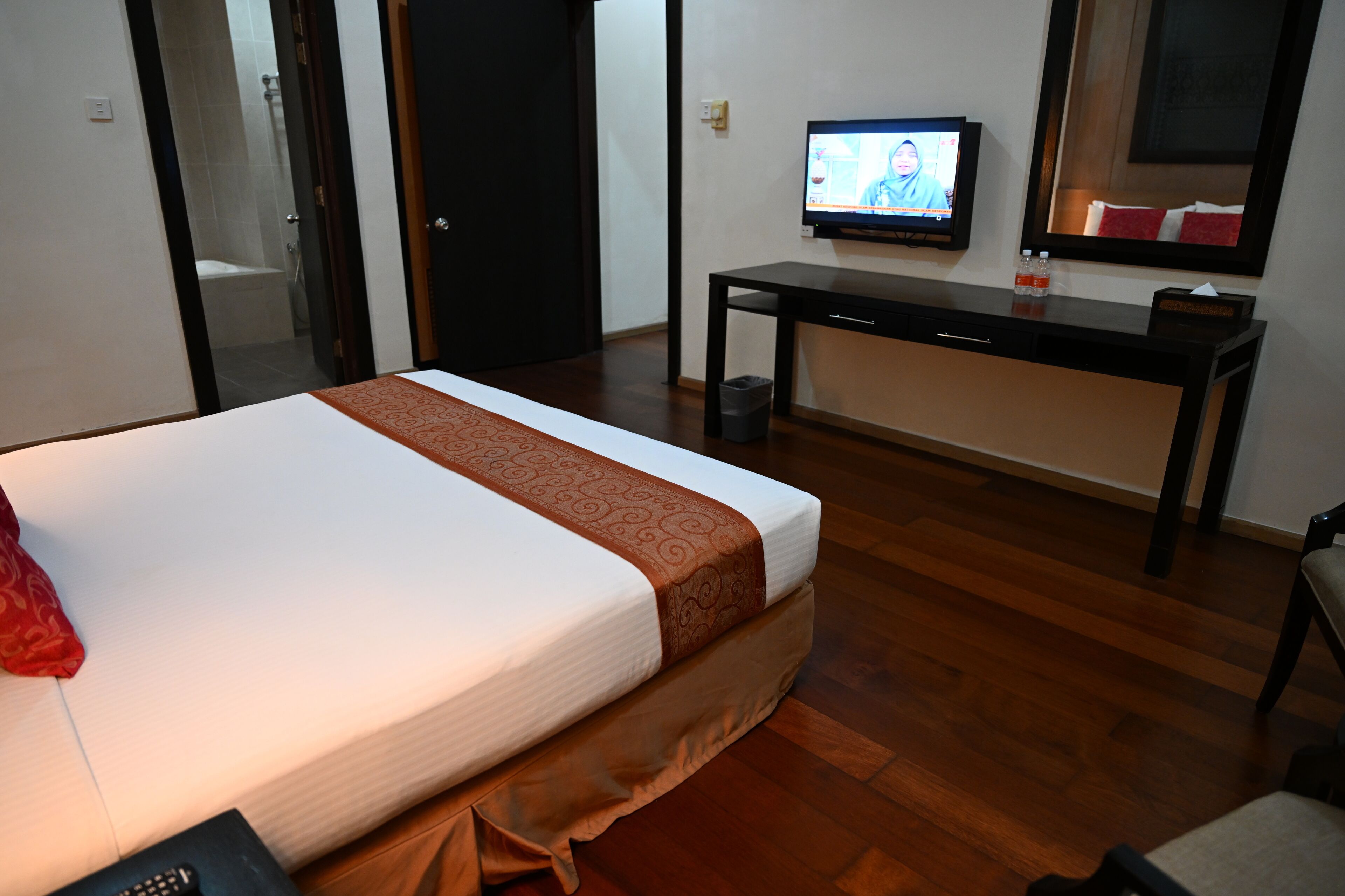 Une chambre d’hôtel avec un lit, un bureau, une télévision et un miroir.