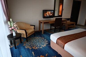 Habitación de hotel con cama, escritorio, silla, televisor y un jarrón con flores.