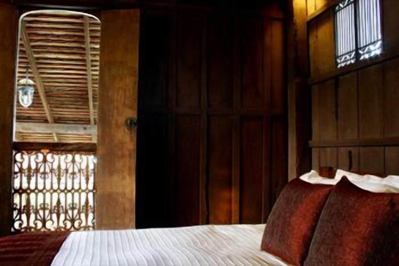 A bedroom with a bed, wooden wardrobe, and a window with a metal grille.