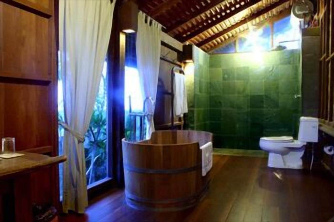 A wooden-floored bathroom with a wooden barrel, a toilet, and a green-tiled shower area.