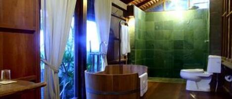 A wooden-floored bathroom with a wooden barrel, a toilet, and a green-tiled shower area.