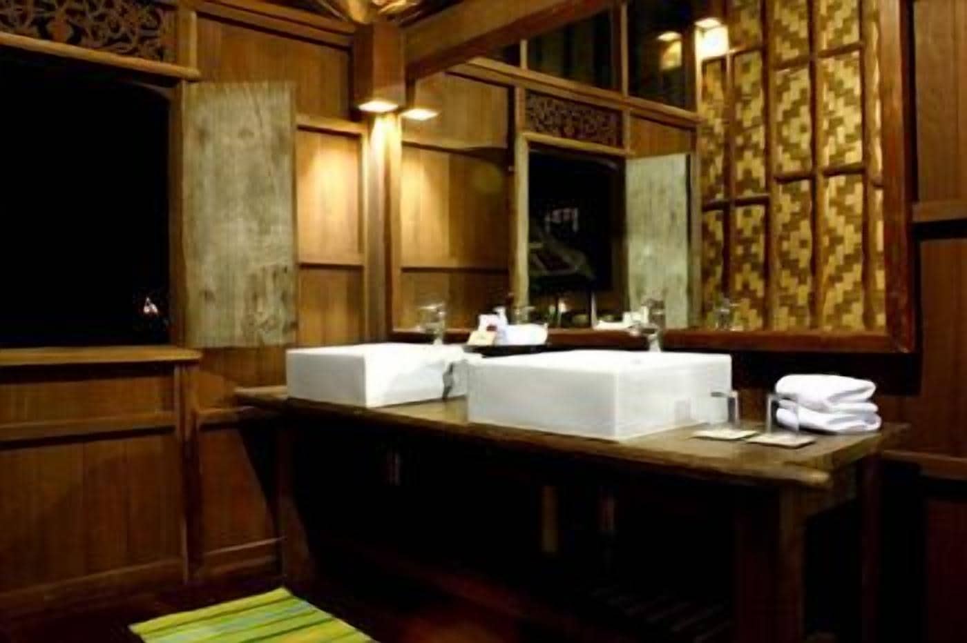 A wooden bathroom with two sinks, a mirror, and a window with patterned curtains.
