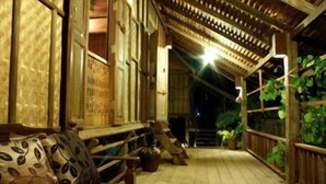 A wooden porch with a bench and potted plants, featuring a traditional architectural style with wooden beams and a tiled floor. - Terrapuri Heritage Village (Setiu)