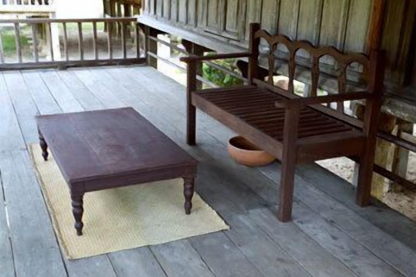 A wooden bench and table on a porch with a woven mat.