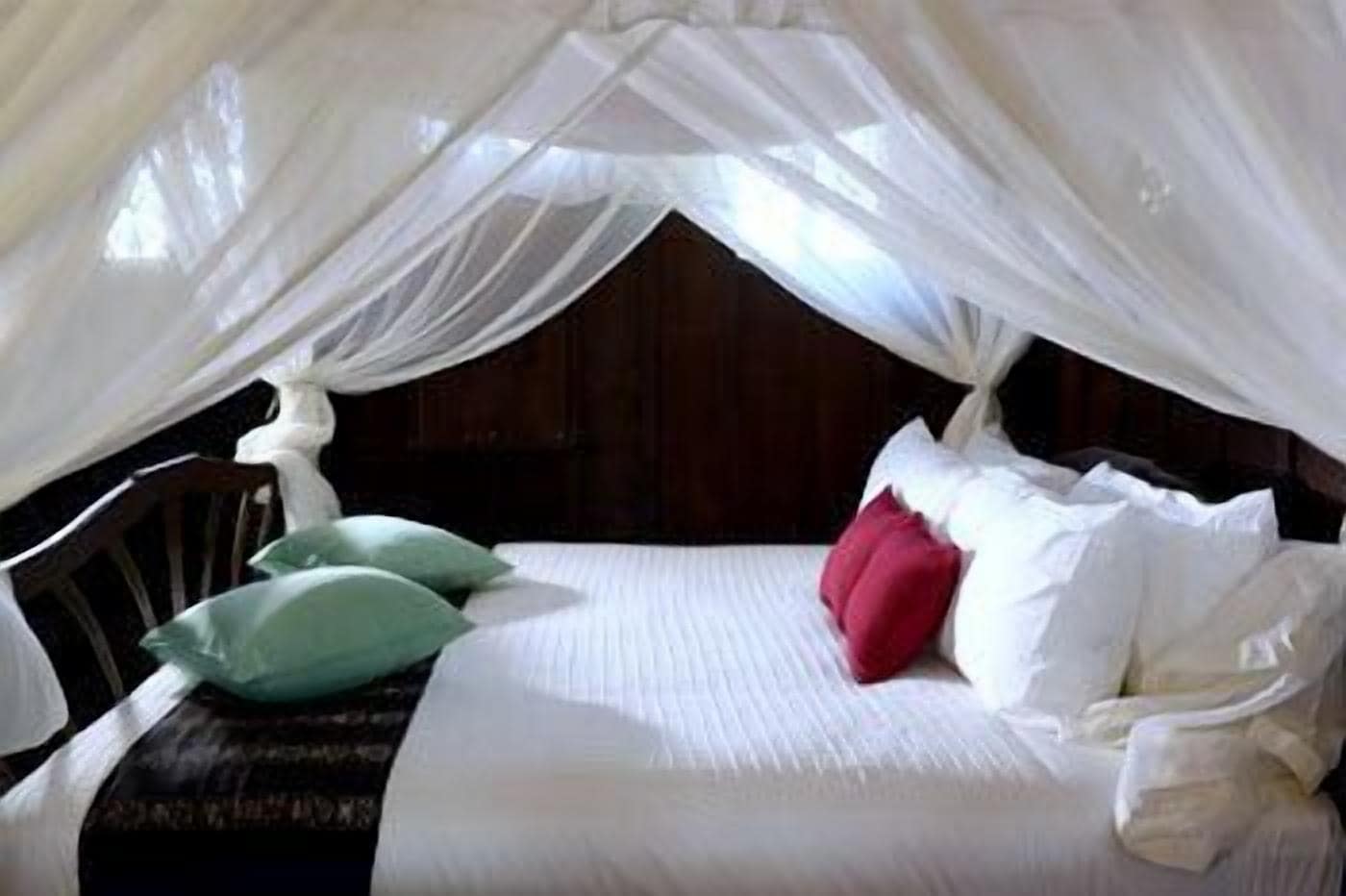 A bed with white bedding, green and red pillows, and a canopy.