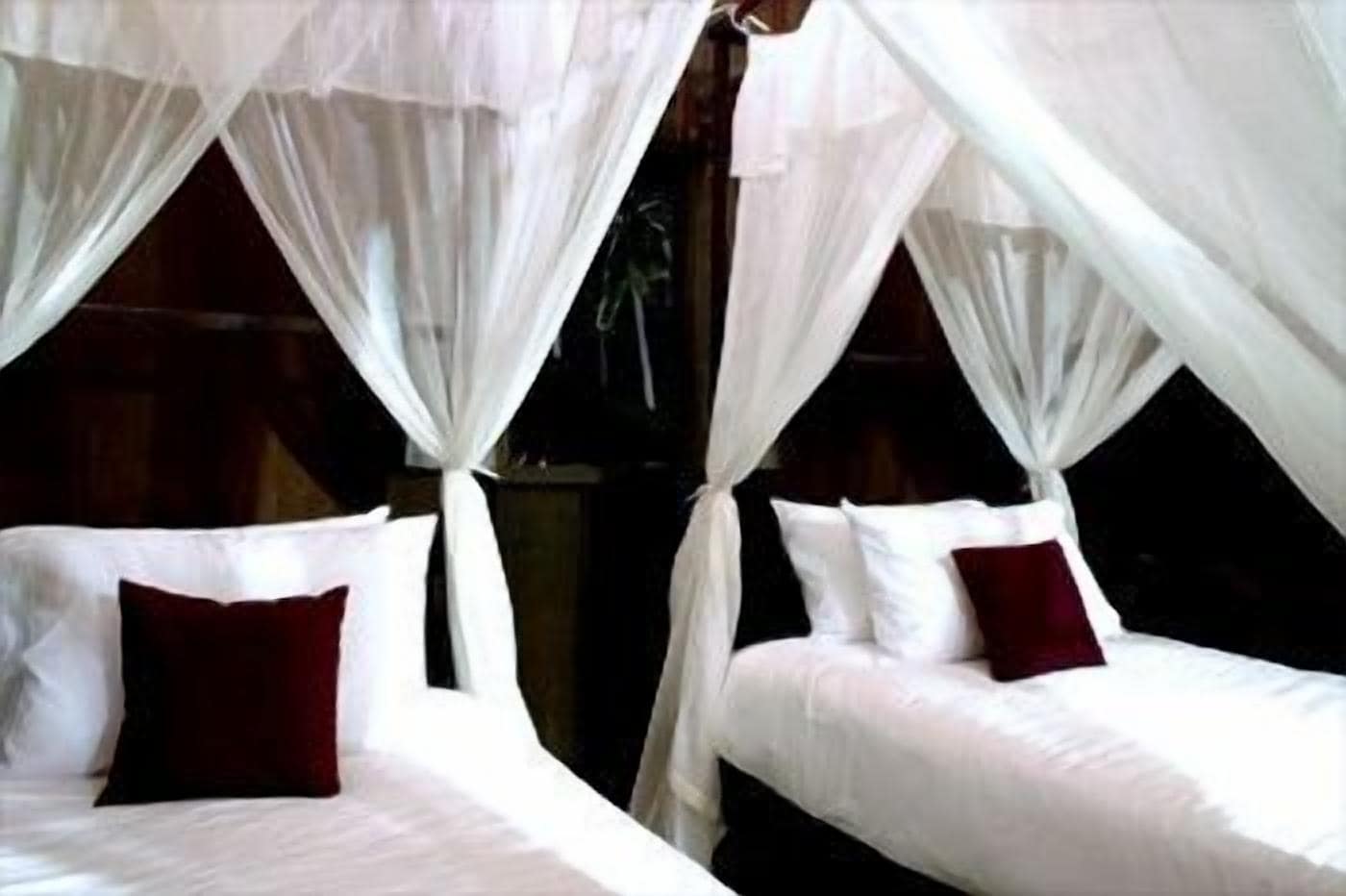A room with two beds, each with white bedding and a red pillow. The beds are separated by a wooden partition.